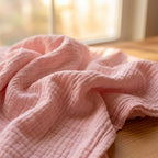 Manta de muselina NubeSuave color Rosa — sobre un banco de madera al borde del lago