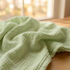 Manta de muselina NubeSuave color Verde salvia — sobre un banco de madera al borde del lago